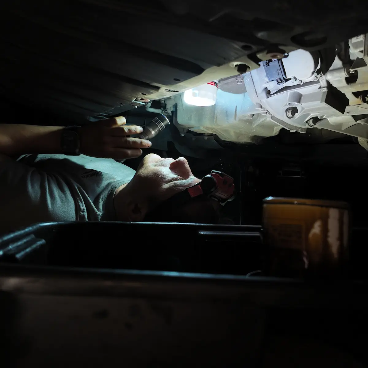Martin working under a car with a flashlight during a nighttime repair